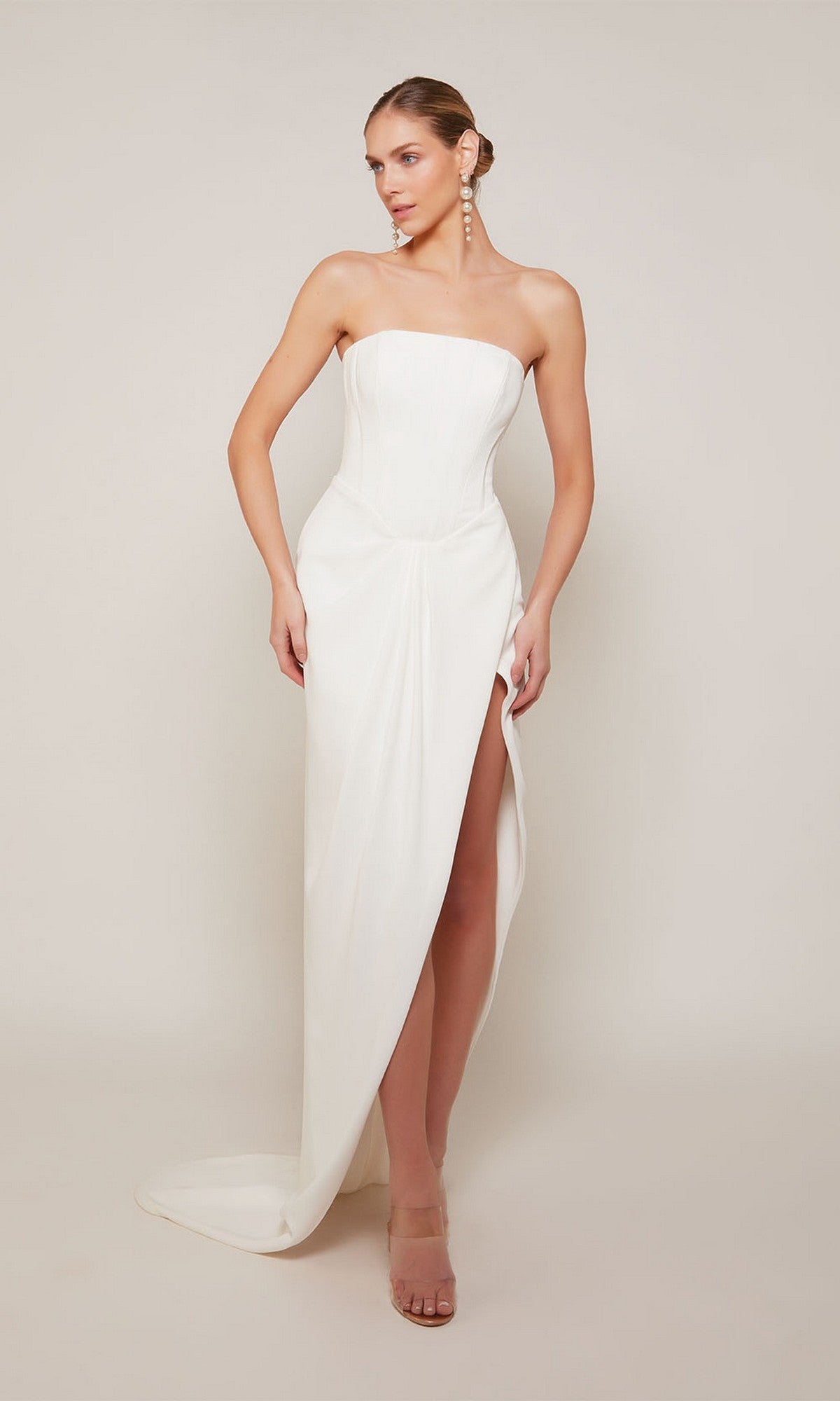 A woman poses against a plain light background wearing the Long Formal Dress: Alyce 70042 in ivory, featuring a strapless corset bodice and a sheath skirt with a thigh-high slit.